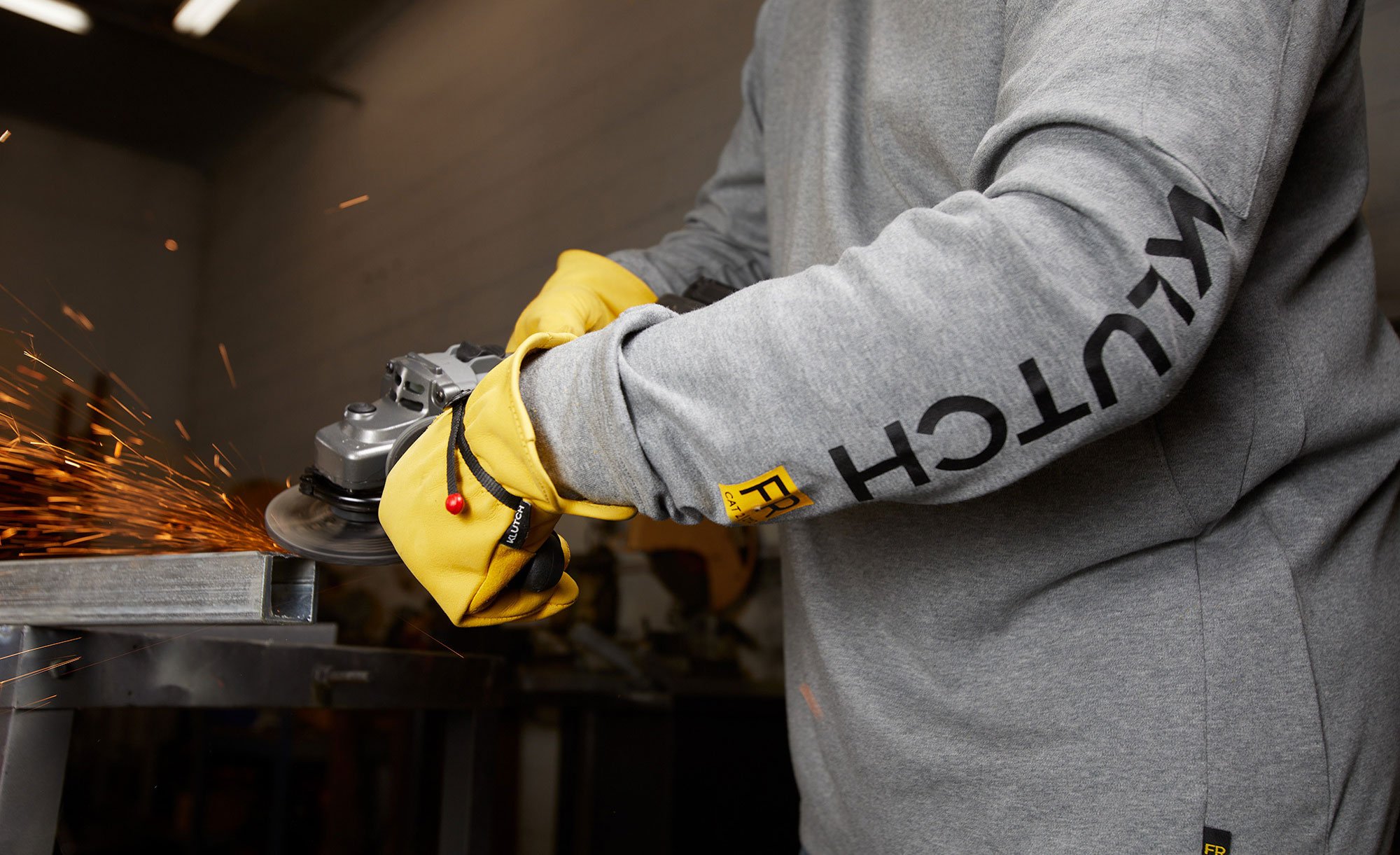 Person wearing a gray Klutch flame-resistant hooded sweatshirt operating an angle grinder.